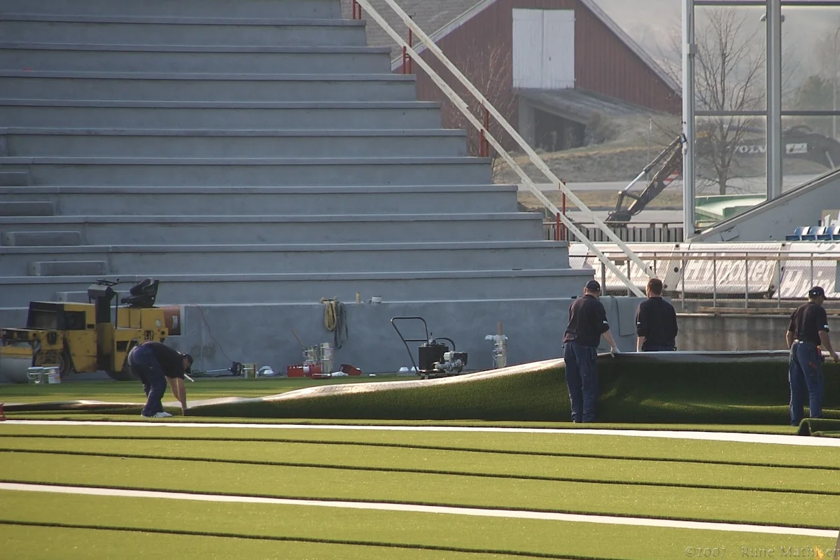Workers laying strips of artificial turf on a stadium field