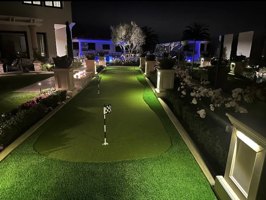 Illuminated backyard putting green with flags at night