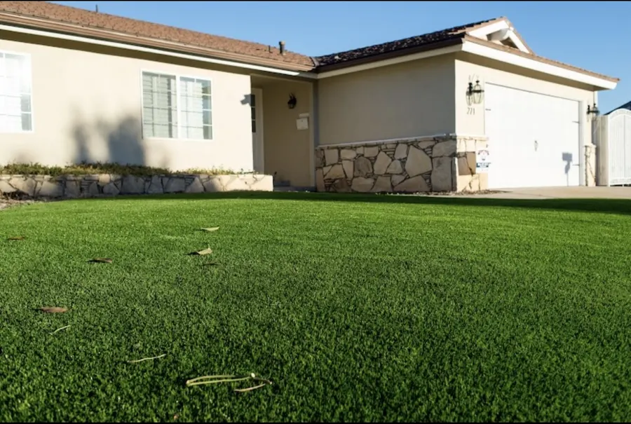 Finished turf lawn beside a light-colored house and paved path