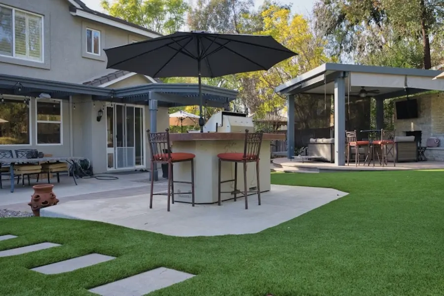 Covered outdoor dining space next to a turf lawn and garden