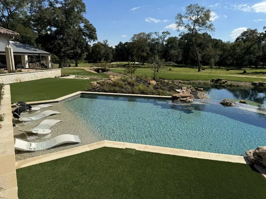Turf surrounding a swimming pool with trees beyond the water
